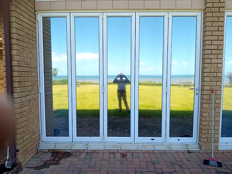Five-panel white aluminium folding doors, closed, on a face-brick patio
