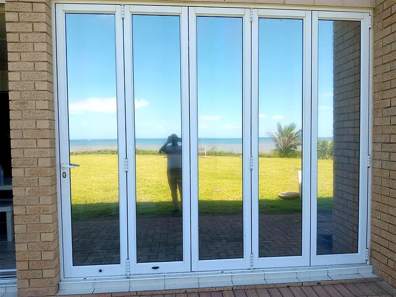 White aluminium folding doors opening a patio onto a sea view